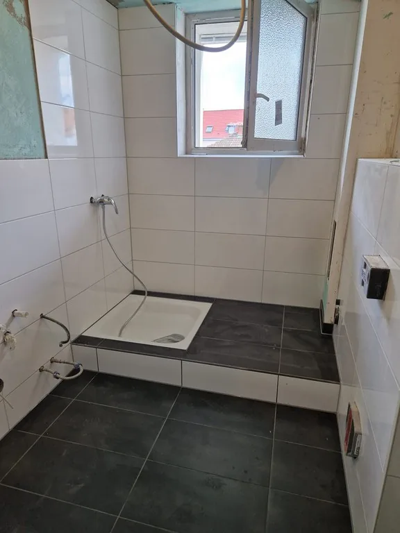 Bad nach der Sanierung – neue Dusche mit anthrazitfarbener Fläche und weißen Wandfliesen